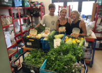 Casper from Goat Grid is stood behind a selection of fresh produce at the Voices in Exile food bank with two other volunteers